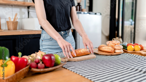 Woman slicing bread with knife on wooden cutting board and prepa photo