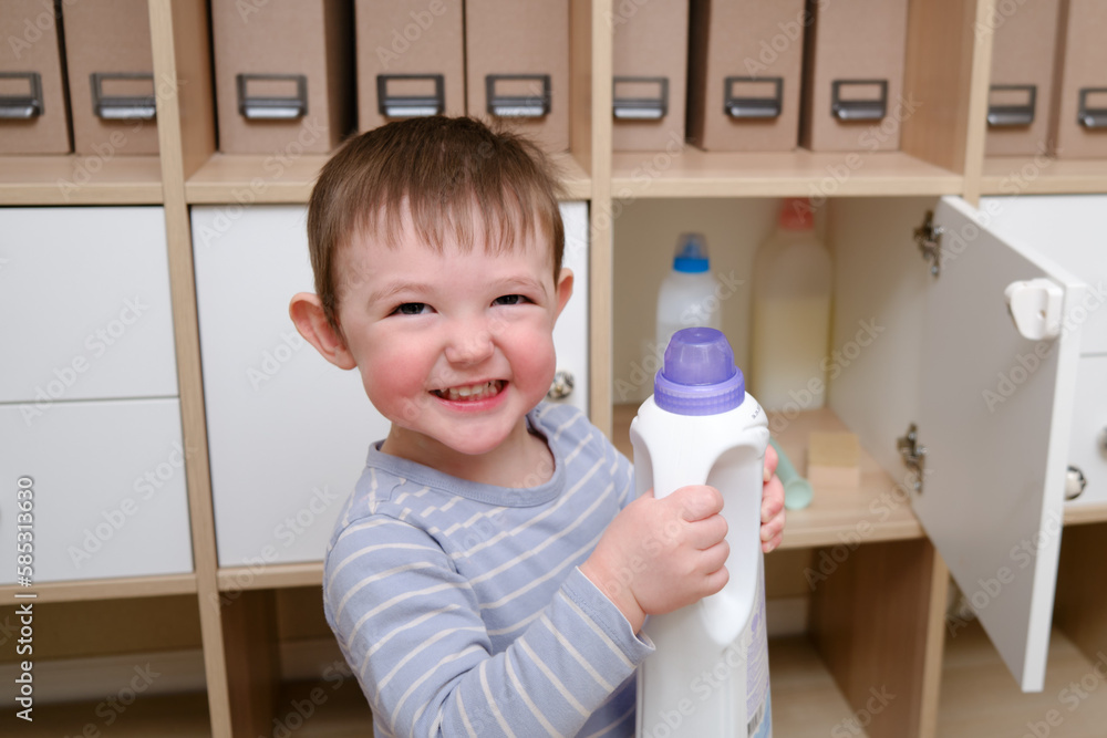 Toddler baby plays with household chemicals and detergent from the closet. Child boy with detergent bottle in home living room. Kid age one year nine months Toddler baby plays with household chemicals and detergent from the closet. Child boy with detergent bottle in home living room. Kid age one year nine months