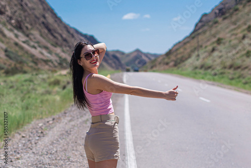 a girl on a desert road in the mountains trying to catch a taxi