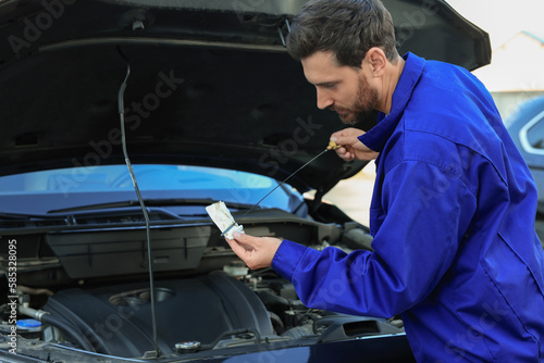 Worker checking motor oil level with dipstick outdoors