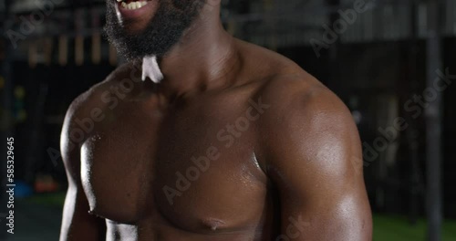 Cropped closeup of strong athletic black Afro African American beadrded smiling man with muscular sweaty torso with chest muscles body care slow motion photo