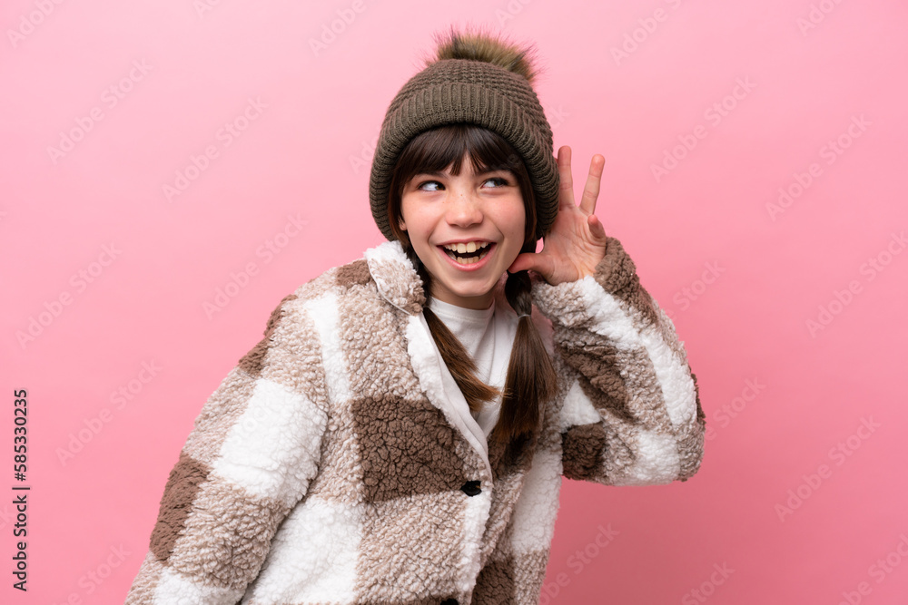 Little caucasian girl with winter jacket isolated on pink background listening to something by putting hand on the ear Little caucasian girl with winter jacket isolated on pink background listening to something by putting hand on the ear
