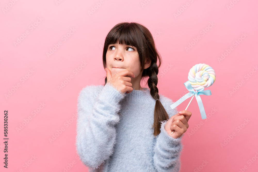 Little caucasian girl holding a lollipop having doubts and thinking Little caucasian girl holding a lollipop having doubts and thinking