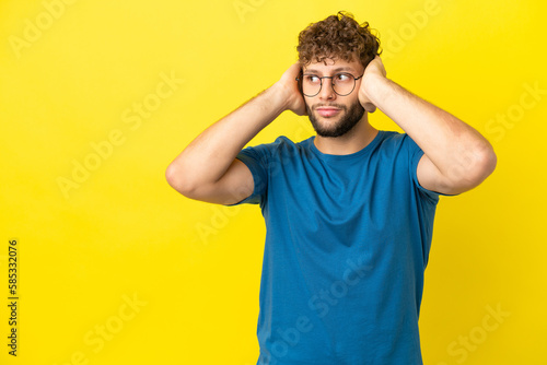 Young handsome caucasian man isolated on yellow background frustrated and covering ears