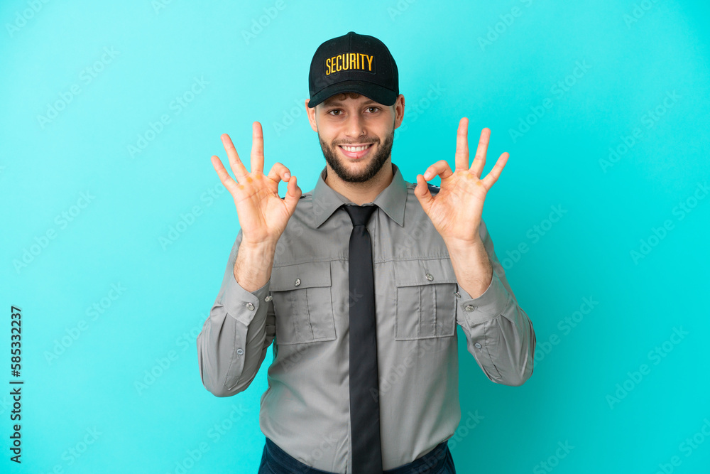 Young security man isolated on blue background showing an ok sign with fingers Young security man isolated on blue background showing an ok sign with fingers