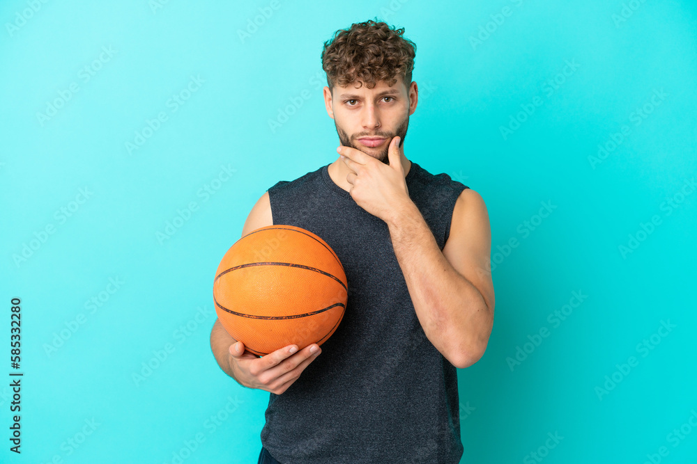Handsome young man playing basketball isolated on blue background thinking