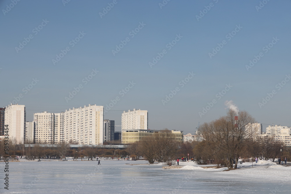 Fototapeta premium Landscapes in the park with melting snow, puddles and ice in spring. Residential buildings and spring landscapes of Butovo, Moscow, thawed patches, March 2023.