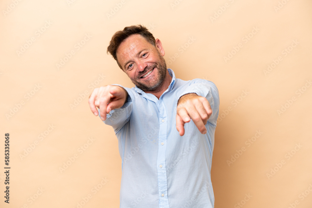 Middle age caucasian man isolated on beige background pointing front with happy expression Middle age caucasian man isolated on beige background pointing front with happy expression