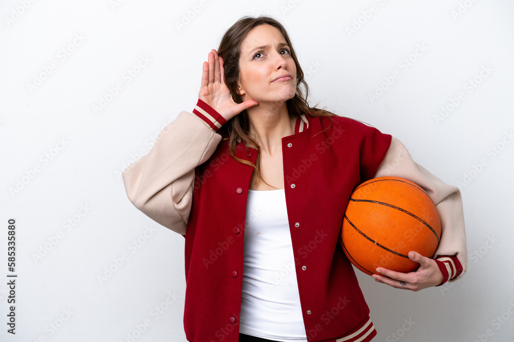 Young caucasian woman playing basketball isolated on white background listening to something by putting hand on the ear Young caucasian woman playing basketball isolated on white background listening to something by putting hand on the ear