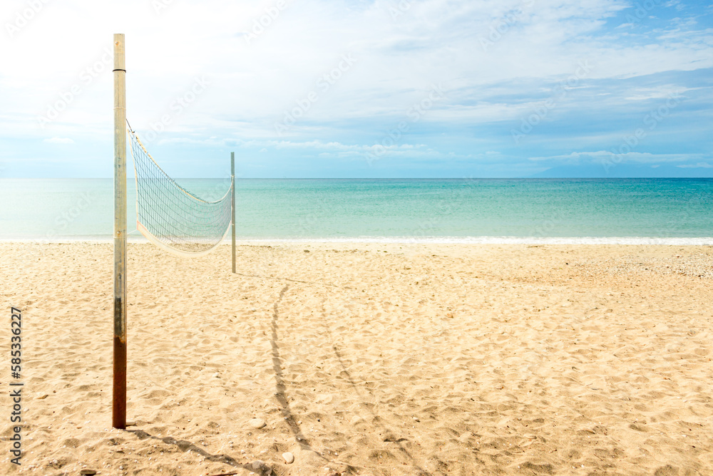 Beach volleyball net on a golden sand beach with turquoise sea waters and bright blue sunny sky