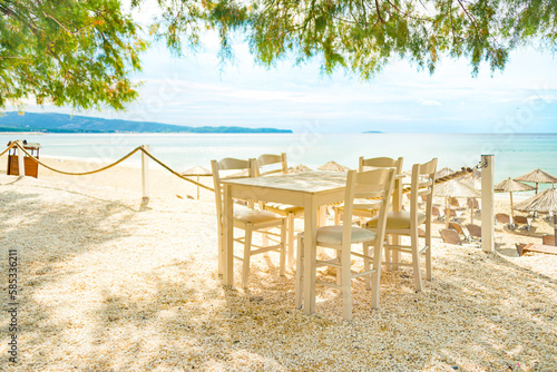 Beach restaurant with all white colored furniture in front of the fascinating golden turquoise colors of the sand and sea. Bright sunny day. photo