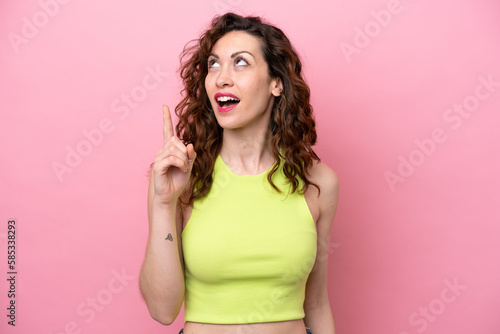 Young caucasian woman isolated on pink background thinking an idea pointing the finger up