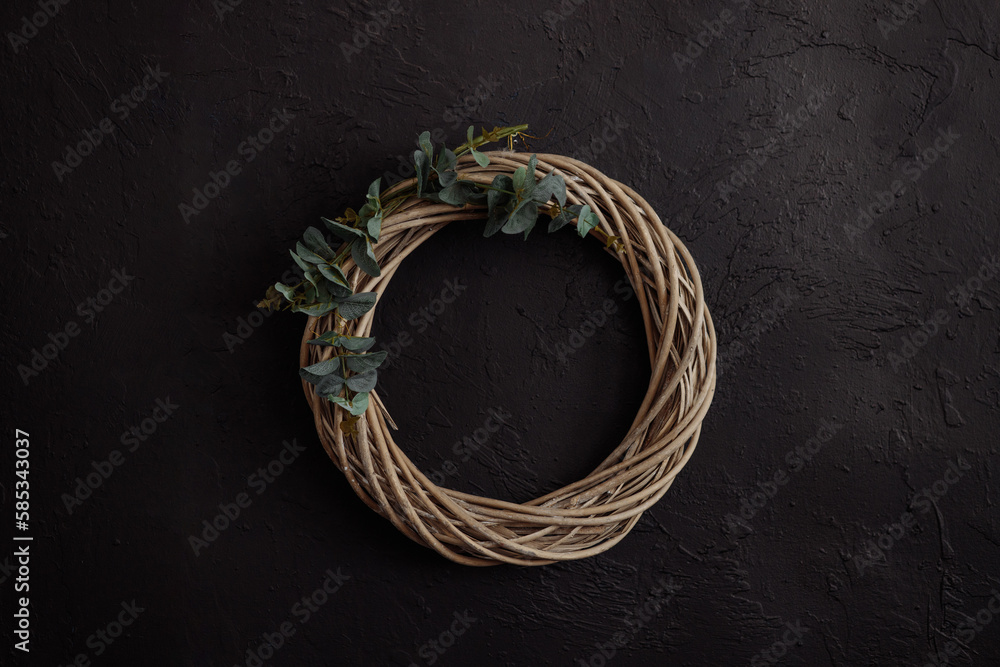 A round vine wreath on a dark background of uneven, shabby, plastered black concrete wall