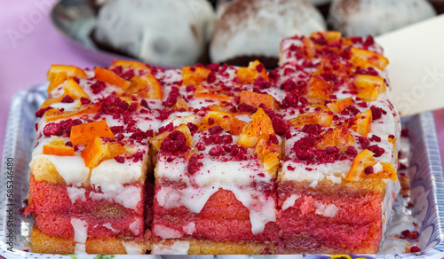Punch cake embellished with pieces of orange and crushed dried raspberries on top, tray with punch desserts on the confectionery stand at farmers street food market in Prague photo
