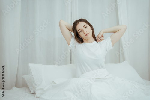 Top view of attractive young smiling woman smiling and stretching while lying on the bed at home