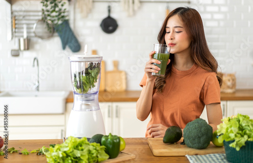 Portrait of beauty healthy asian woman making green vegetables detox vegan and green fruit smoothie with blender.young girl drinking glass of green fruit smoothie in kitchen.Diet concept.healthy
