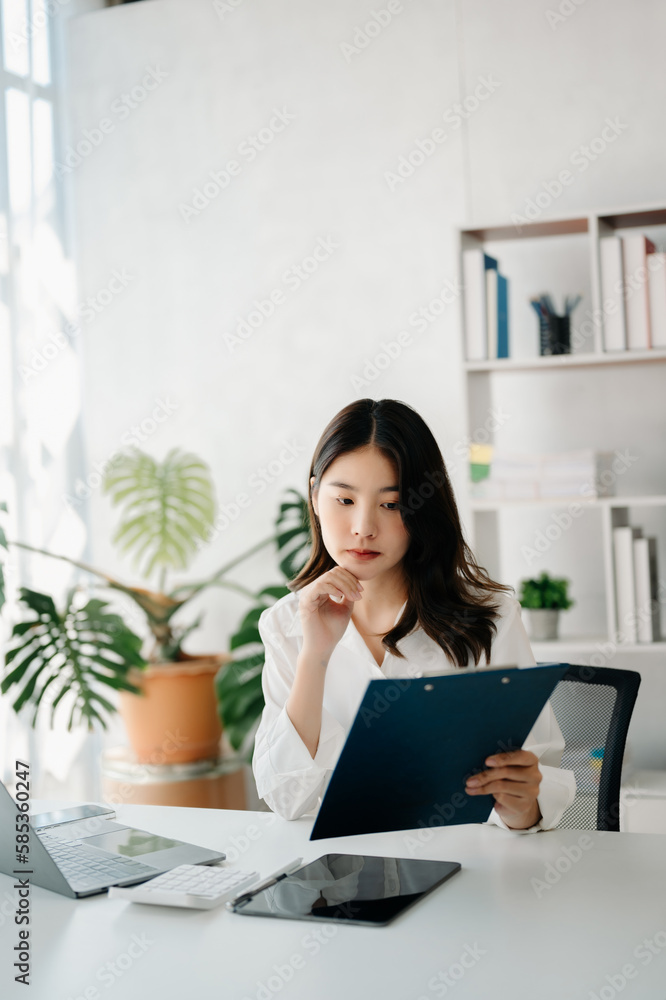 Confident Asian woman with a smile standing holding notepad and tablet at the modern office. Confident Asian woman with a smile standing holding notepad and tablet at the modern office.