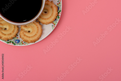 Filiżanka z mocną kawą po lewej stronie zdjęcia na różowym tle, na spodku leżą ciasteczka