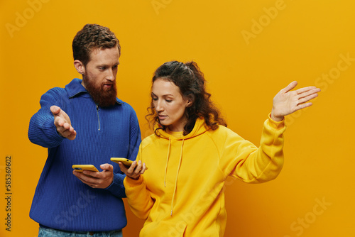 Woman man cheerful couple with phones in hand social networking and communication crooked smile fun and fight, in yellow background. The concept of real family relationships, freelancers, work online.