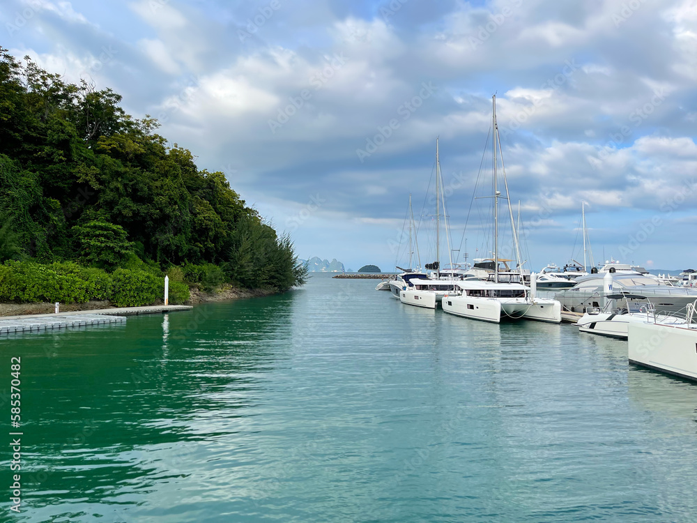 Luxury boats in the marina. Yachts in the harbor. Sailboats anchored in the sea bay. Beautiful water of bright emerald color. Hilly coast, green forest. Lowered sails. Cruise. Blue sky, amazing clouds
