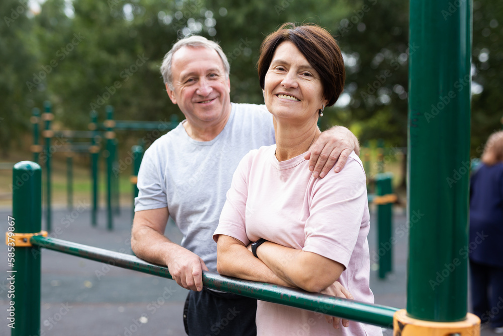 Portrait of an elderly couple in sportswear on sports ground in a city park on summer day