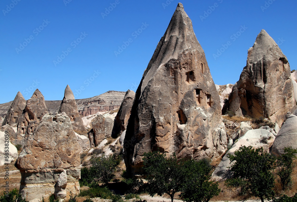 Landscape with mushroom-shaped mountains (also called Fairy Chimneys) with caves inside against a bright blue clear sky in the Rose Valley between the towns of Goreme and Cavusin in Cappadocia, Turkey