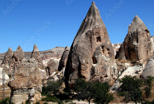 Landscape with mushroom-shaped mountains (also called Fairy Chimneys) with caves inside against a bright blue clear sky in the Rose Valley between the towns of Goreme and Cavusin in Cappadocia, Turkey
