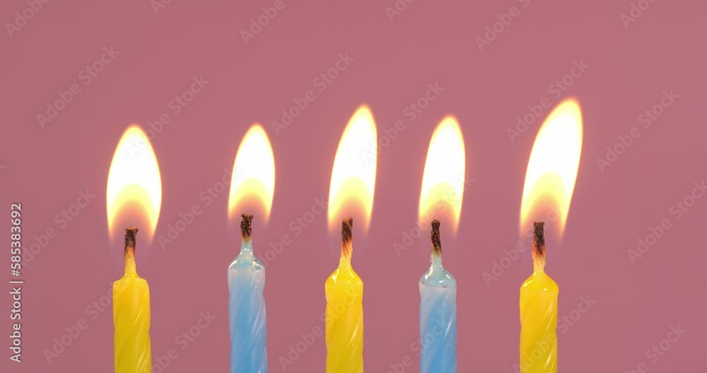 Blowing out yellow and light blue festive candles on pink background, closeup Blowing out yellow and light blue festive candles on pink background, closeup