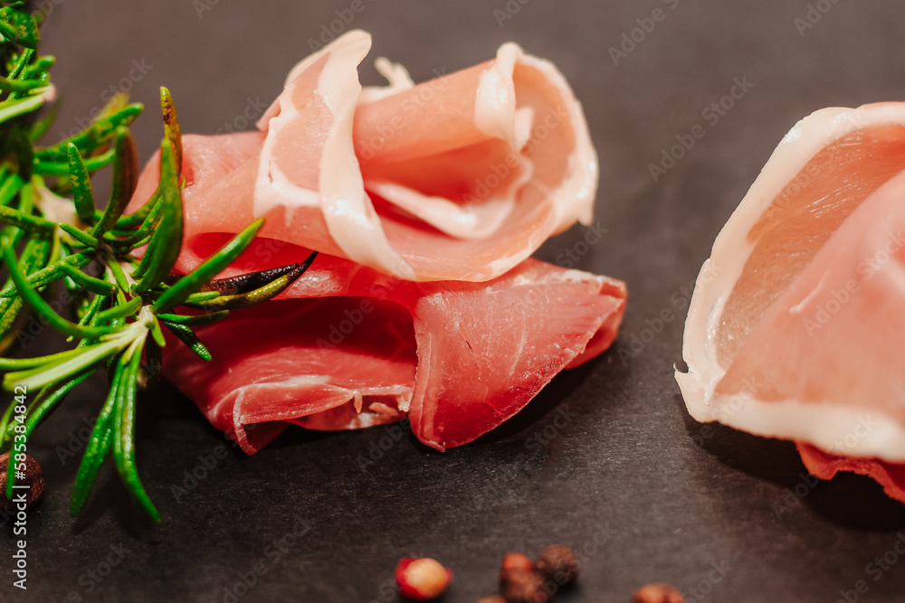 Pieces of dried pork jamon prosciutto with rosemary on a black board.