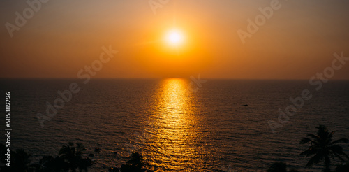 A bright misty sunset over the endless sea. Bright sunny path on the water and silhouettes of palm trees. Postcard view of a vacation near the sea, romantic meetings, background for travel