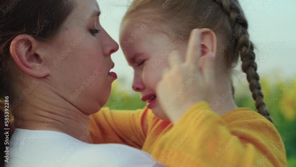 Baby cries mom hugs child in summer park. Tender mother soothes her