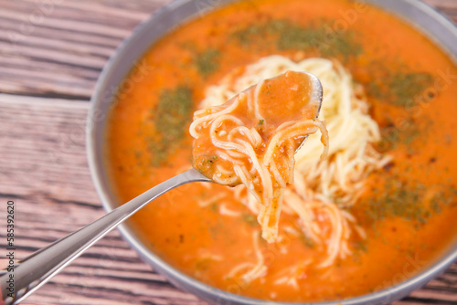 Tomato soup with noodles being eaten with spoon on a wooden background 