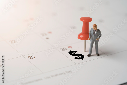 фотографія Businessman figure and red pin with dollar sign on calendar for plan and appointment of employee  salary payment concept