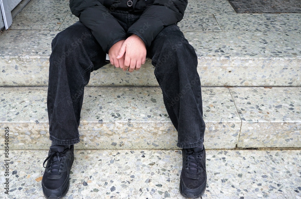 Jugendlicher mit schwarzen Turnschuhen, Hose, und Pullover sitzt auf Steintreppe Jugendlicher mit schwarzen Turnschuhen, Hose, und Pullover sitzt auf Steintreppe
