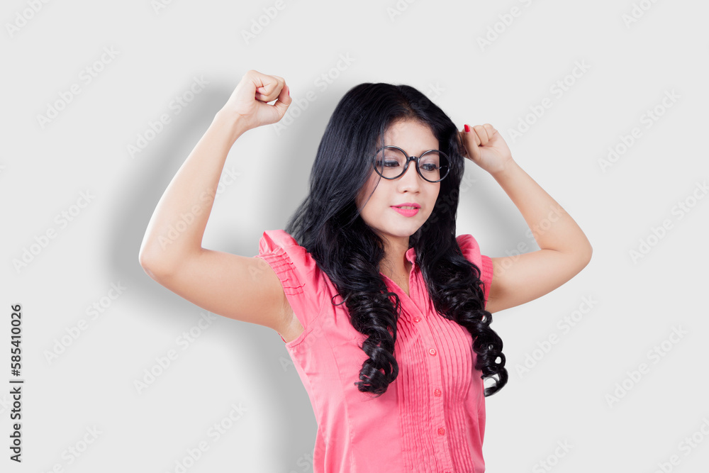 Woman with glasses raises hands and shows muscles over white background Woman with glasses raises hands and shows muscles over white background