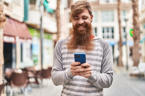 Young redhead man smiling confident using smartphone at street © Krakenimages.com