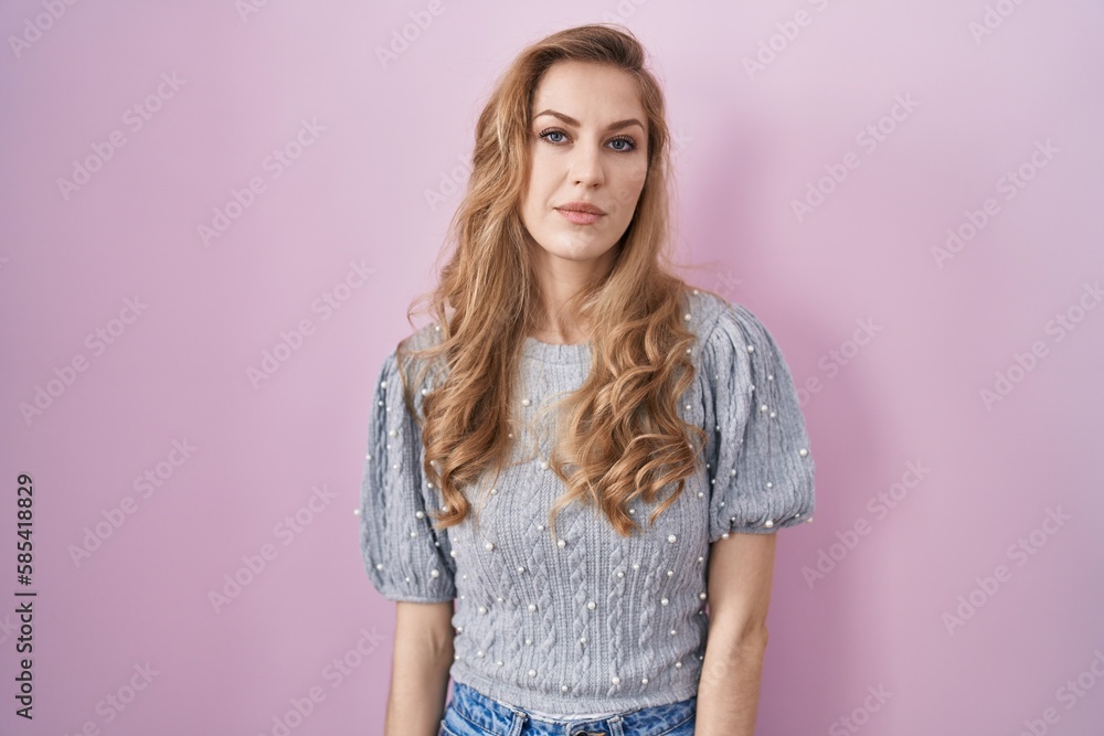 Beautiful blonde woman standing over pink background relaxed with serious expression on face. simple and natural looking at the camera. Beautiful blonde woman standing over pink background relaxed with serious expression on face. simple and natural looking at the camera.