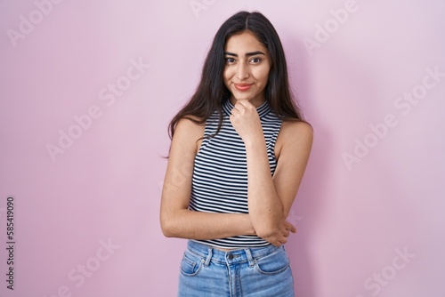 Young teenager girl wearing casual striped t shirt looking confident at the camera smiling with crossed arms and hand raised on chin. thinking positive.