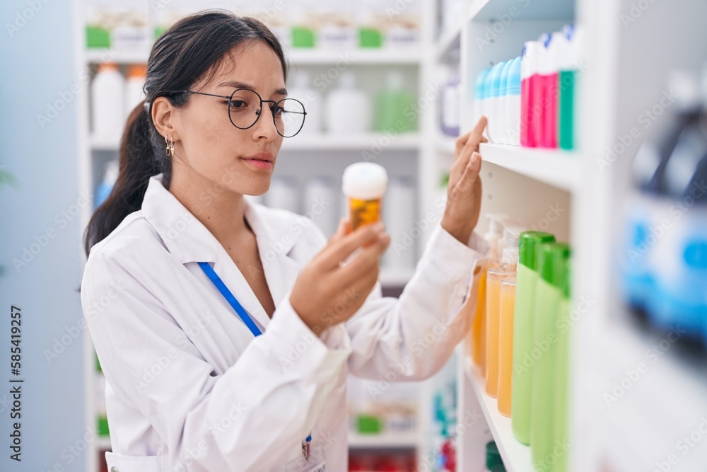 Young beautiful hispanic woman pharmacist holding pills bottle at pharmacy