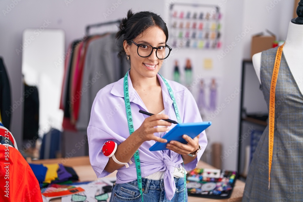 Young beautiful hispanic woman tailor smiling confident using touchpad at tailor shop