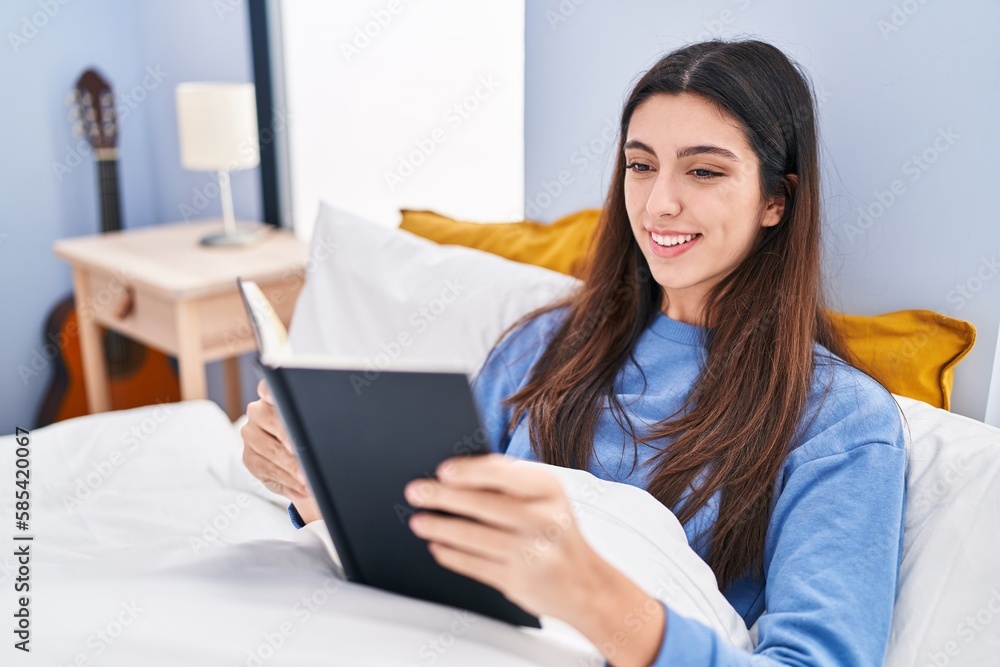 Young beautiful hispanic woman reading book sitting on bed at bedroom Young beautiful hispanic woman reading book sitting on bed at bedroom