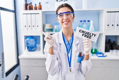 Young beautiful woman working on cruelty free laboratory smiling happy pointing with hand and finger to the side