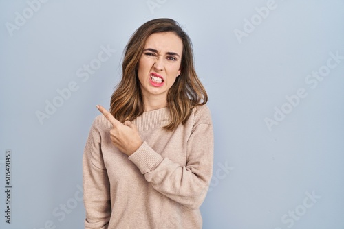Young woman standing over isolated background pointing aside worried and nervous with forefinger, concerned and surprised expression