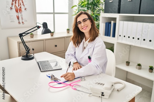 Young woman wearing doctor uniform writing medical report at clinic