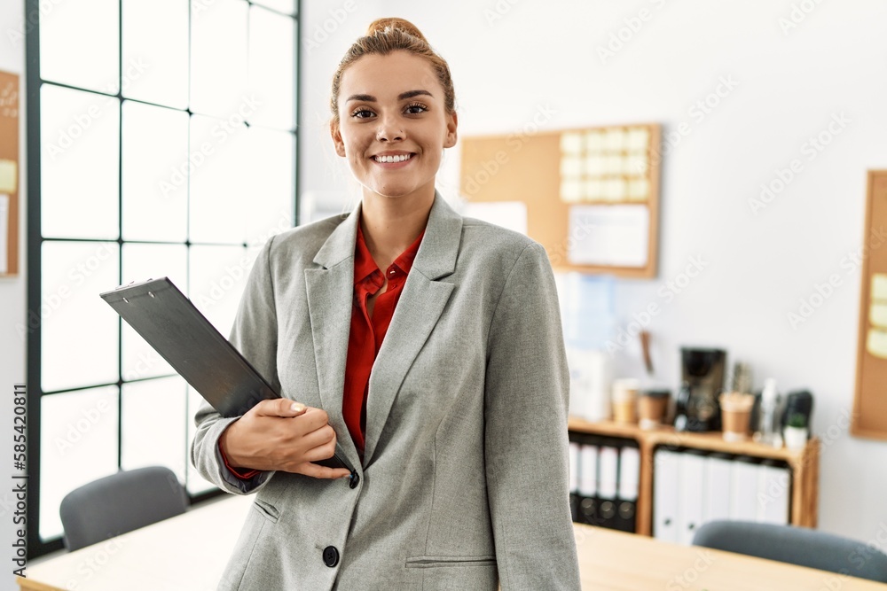 Young woman business worker smiling confident holding clipboard at office Young woman business worker smiling confident holding clipboard at office