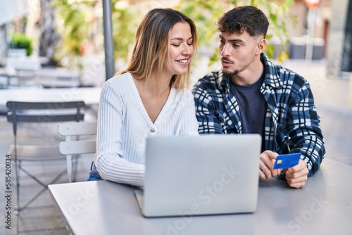 Young man and woman couple using laptop and credit card sitting on table at coffee shop terrace