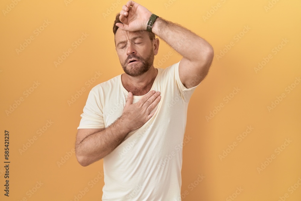 Middle age man with beard standing over yellow background touching forehead for illness and fever, flu and cold, virus sick Middle age man with beard standing over yellow background touching forehead for illness and fever, flu and cold, virus sick