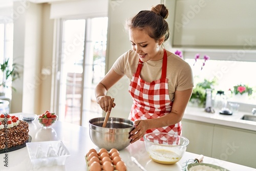 Young beautiful hispanic woman smiling confident mixing chocolate on bowl at the kitchen