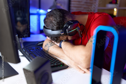 Young hispanic man streamer stressed using computer at gaming room