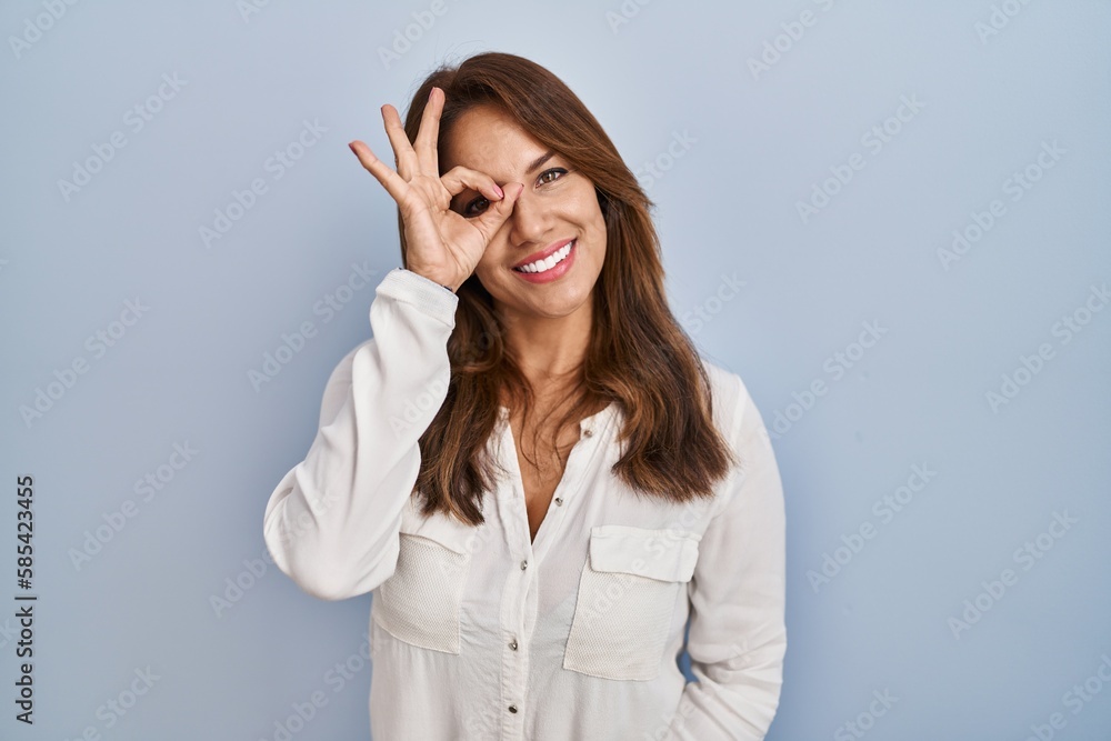 Hispanic woman standing over isolated background doing ok gesture with hand smiling, eye looking through fingers with happy face. Hispanic woman standing over isolated background doing ok gesture with hand smiling, eye looking through fingers with happy face.